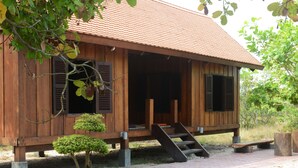 A wooden house with a tiled roof, a staircase leading to the entrance, and a small tree in front. - Dracaena Resort (Prasat Sambour)