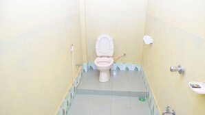 A small, narrow bathroom with a toilet, a blue bucket, and a white sink. - Green Palace Tea Resort (Kamalganj)