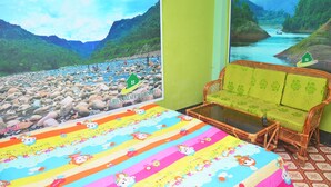 A room with a bed, a sofa, and two large windows with scenic river views. - Green Palace Tea Resort (Kamalganj)