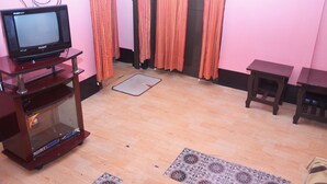 Un salon avec un téléviseur à écran plat posé sur un meuble en bois, une petite table en bois et un tapis à motifs sur le plancher en bois.