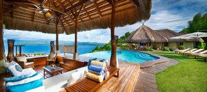 A poolside area with wooden deck, lounge chairs, and a thatched-roof structure. - Pure Shores Villa (Guindulman)