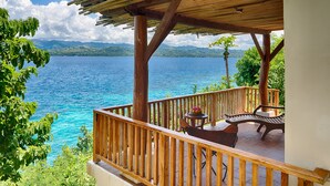 A wooden deck with a view of a large body of water and mountains in the background. - Pure Shores Villa (Guindulman)