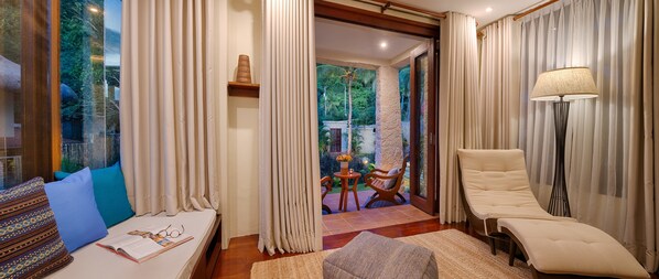 A well-lit room with a bed, a reading area with a table and chairs, a lounge chair, and a lamp. - Pure Shores Villa (Guindulman)