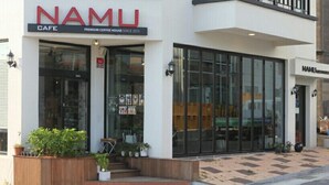 Un edificio moderno con un café llamado Namu, con amplios ventanales y un diseño limpio y minimalista.