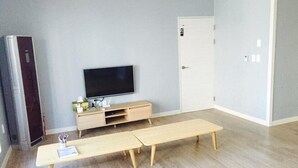 Una habitación con una televisión sobre un mueble de madera, un banco, un armario y una puerta con un número.