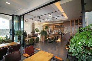 A modern cafe with wooden tables and chairs, a bar area, and indoor plants. - Namu Guesthouse & Pension - Hostel (Yeosu)