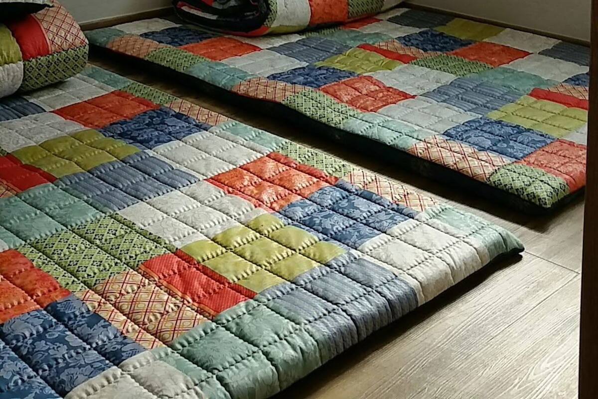 Una habitación pequeña con dos camas, una ventana con persianas y un enchufe en la pared.