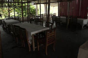 Een restaurant met tafels en stoelen, geplaatst onder een overdekte ruimte met grote ramen.