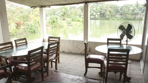 A covered outdoor dining area with a table and chairs, a fan, and a view of a water body.