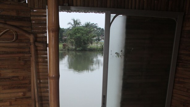 A room with a bed, a wooden door, and a view of a calm body of water.