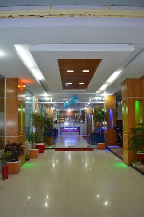 A hotel lobby with a reception desk, potted plants, and a blue dolphin sculpture on the ceiling.