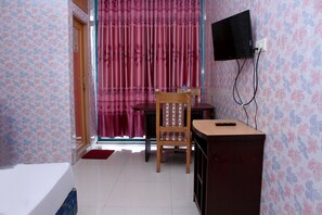 A room with a bed, a desk with a chair, a television mounted on the wall, and a window with curtains.