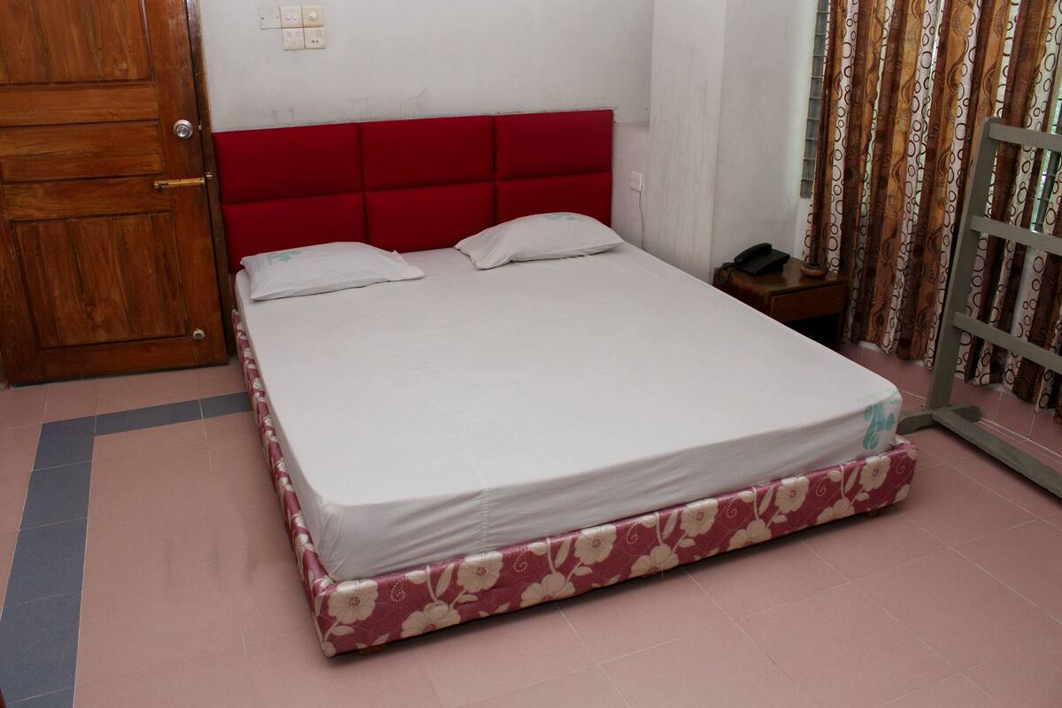 A bed with a red headboard, a floral-patterned mattress, and a wooden door to the left.