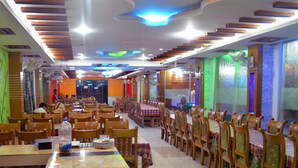A spacious dining area with long tables and wooden chairs, equipped with ceiling fans and ambient lighting. - Saint Martin Resort (Cox's Bazar)