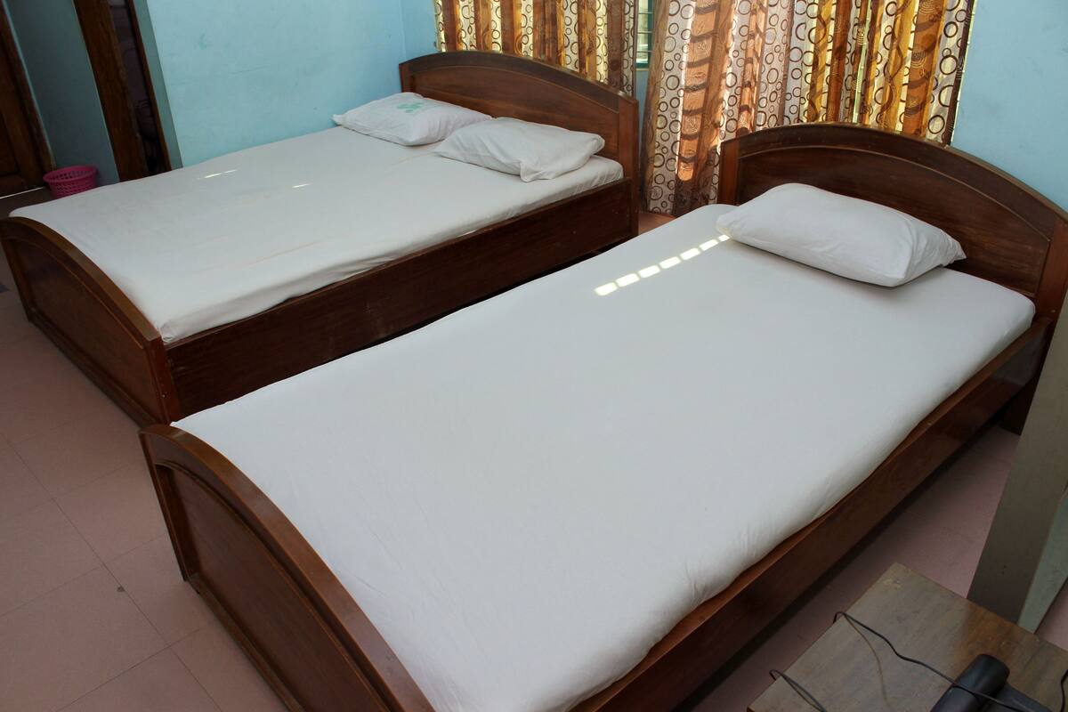 Two wooden beds with white bedding in a room with patterned curtains.