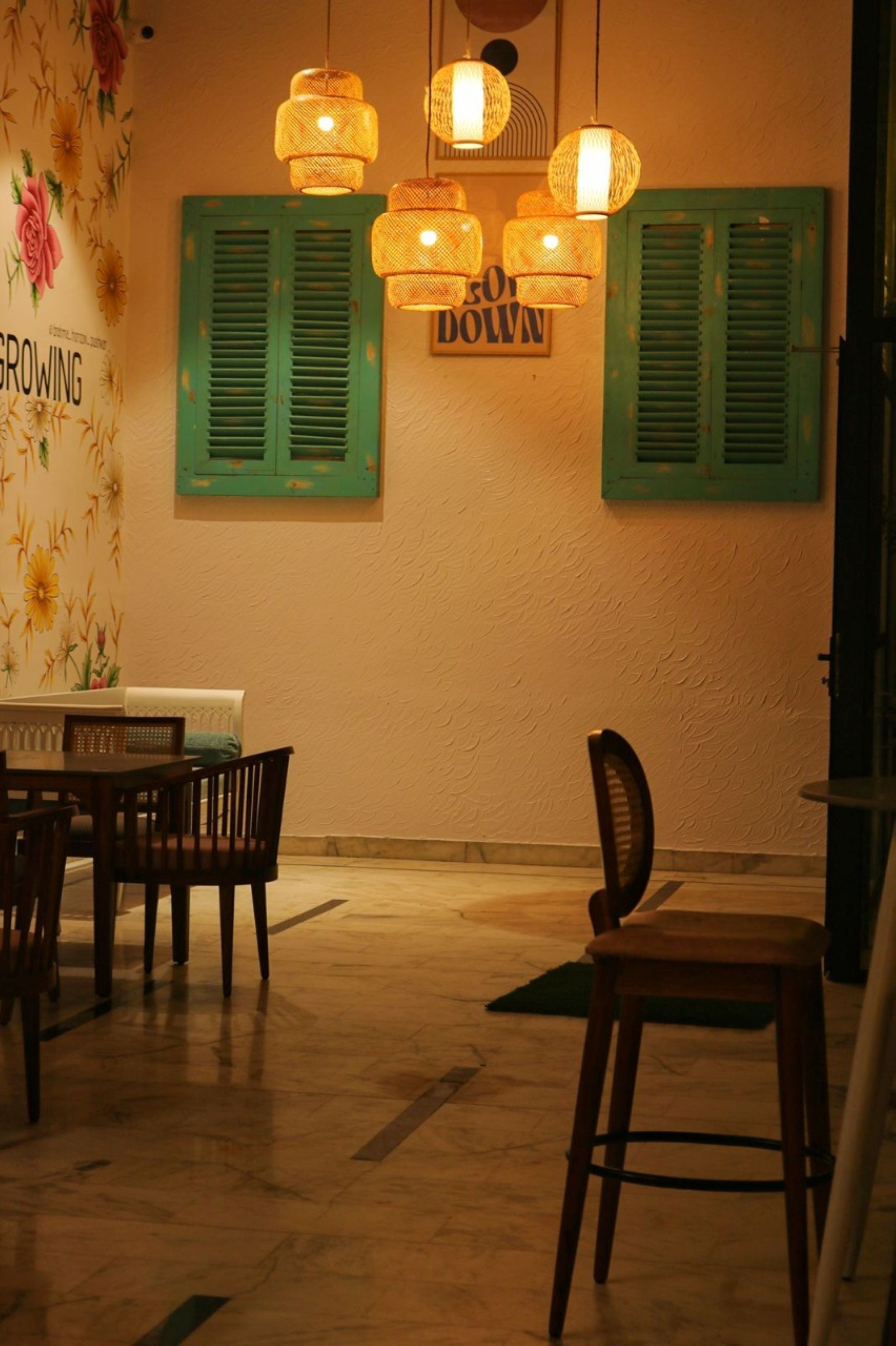 Uma sala de jantar com mesa e cadeiras, persianas verdes e luminárias de vime suspensas.