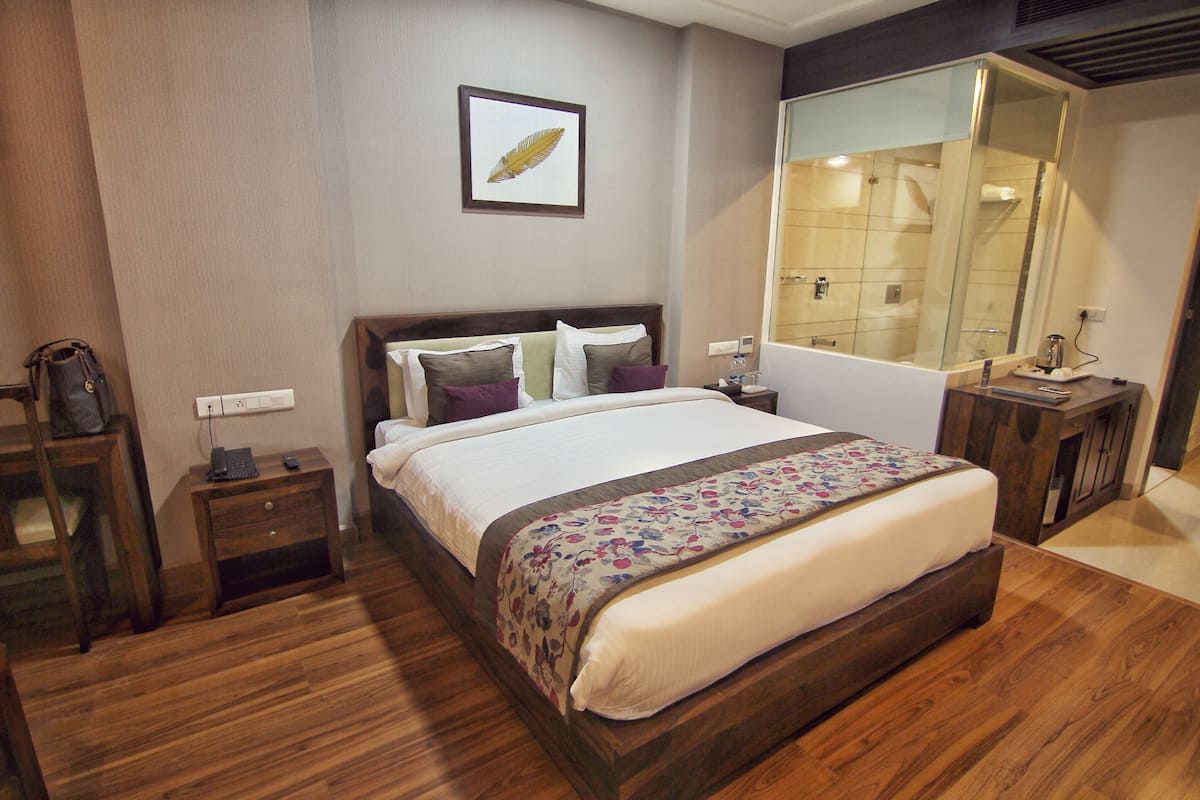 Habitación de hotel con una cama grande, una mesita de noche de madera, un tocador, un espejo y una zona de ducha.