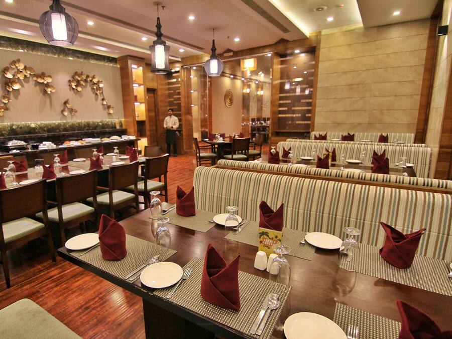 Un comedor con varias mesas dispuestas para el servicio, una barra de buffet y una zona de estar con bancos acolchados.
