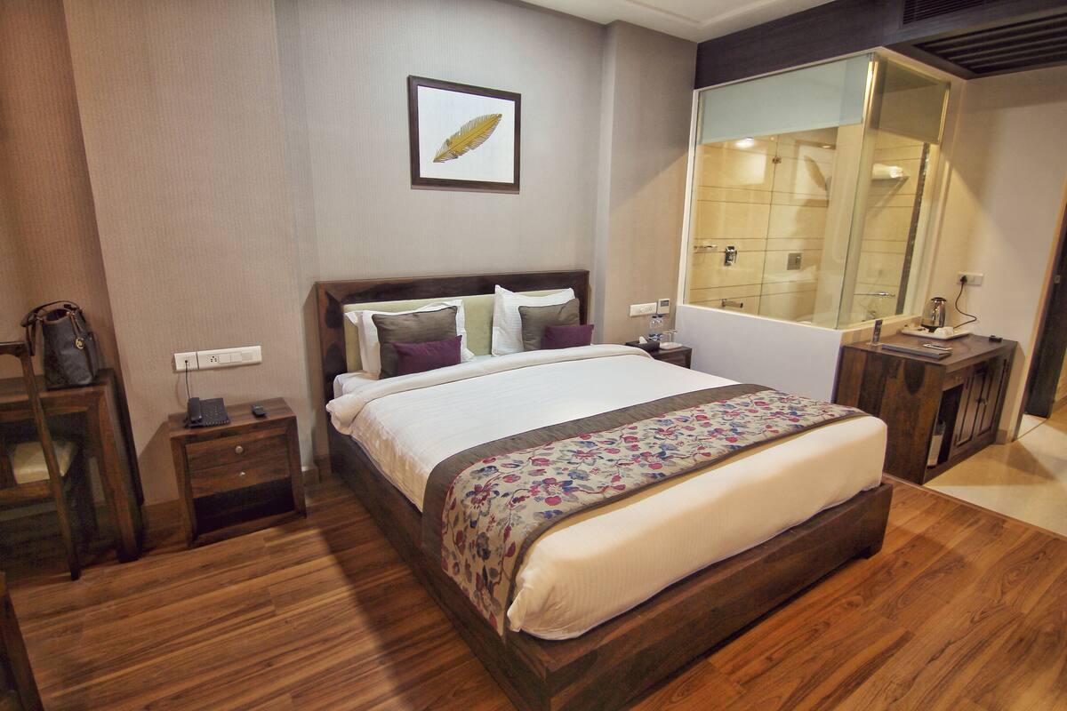Habitación de hotel ordenada con una cama grande, una mesita de noche, un espejo y suelo de madera.