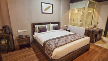 A neatly arranged hotel room with a large bed, a bedside table, a nightstand, a mirror, and a wooden floor.
