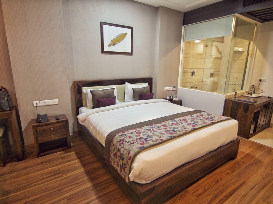 A neatly arranged hotel room with a large bed, a bedside table, a nightstand, a mirror, and a wooden floor.