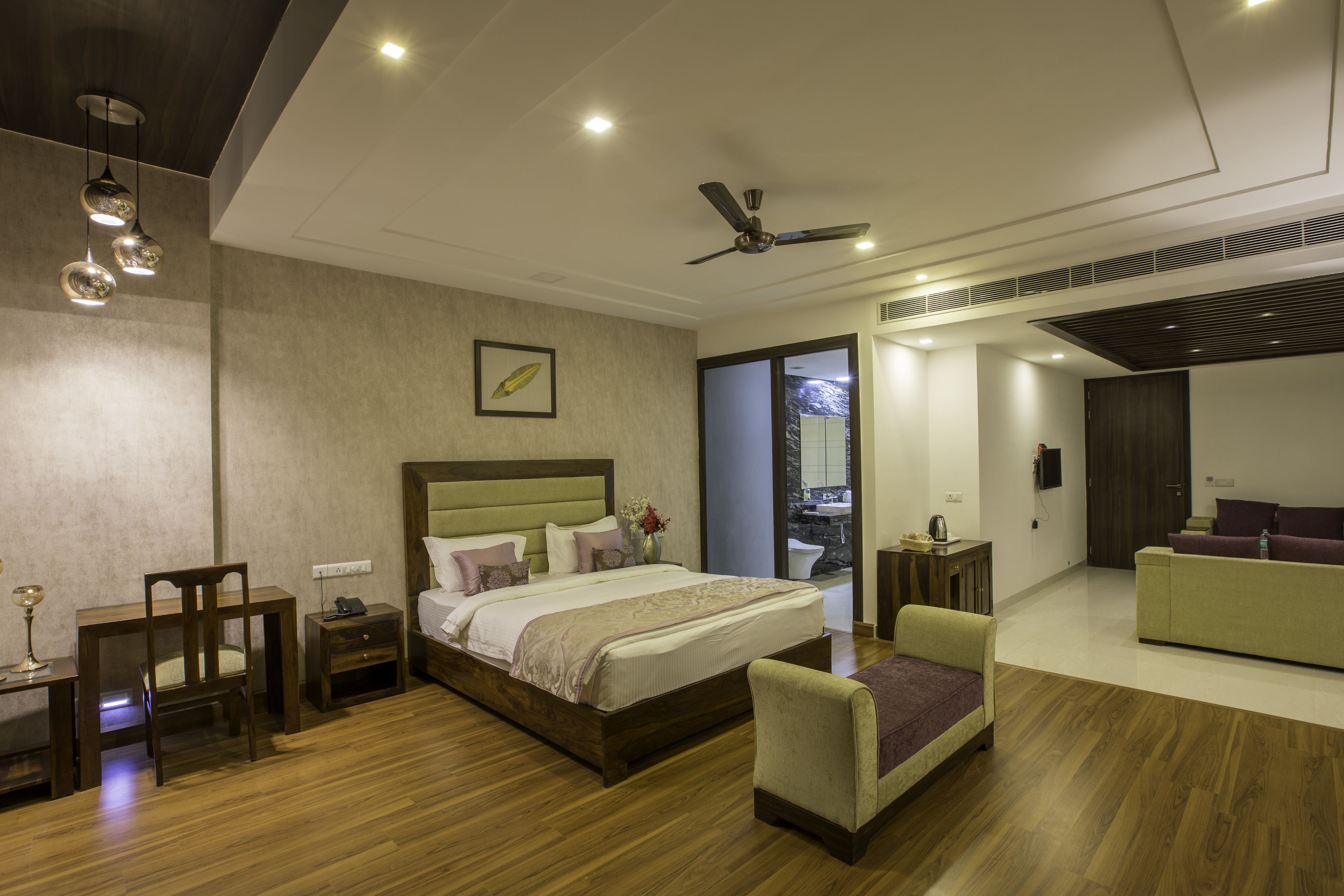 A modern bedroom with a large bed, bedside tables, a chair, a sofa, and a ceiling fan.