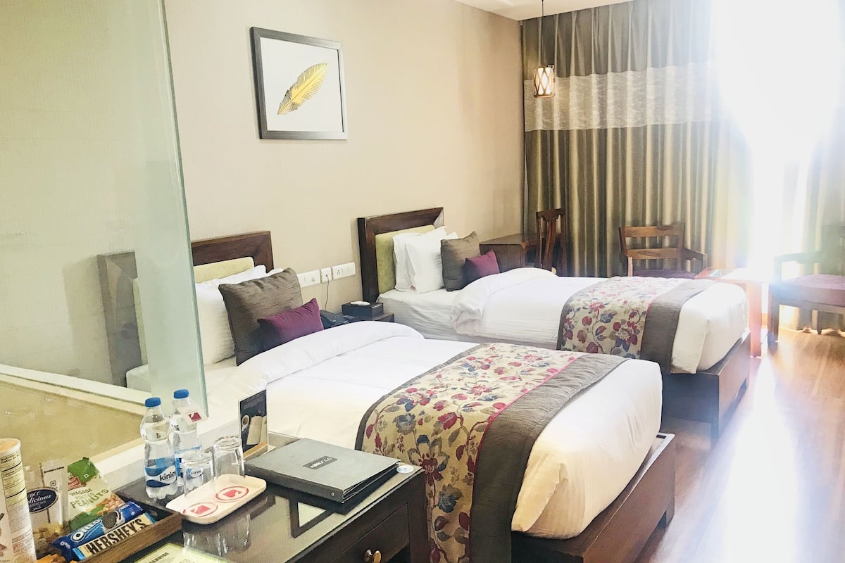 Habitación de hotel con dos camas, una mesita de noche con una bandeja de aperitivos, un espejo y una ventana con cortinas.