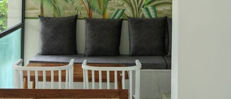 Una habitación con un mural de palmeras, un banco blanco y una silla de mimbre.