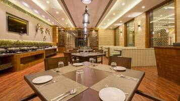 A restaurant with a long counter, multiple tables, and a high ceiling with recessed lighting.