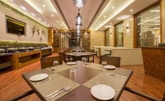 A restaurant with a long counter, multiple tables, and a high ceiling with recessed lighting.