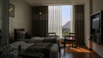 A hotel room with two beds, a TV, a desk with a laptop, and a view of mountains through large windows.