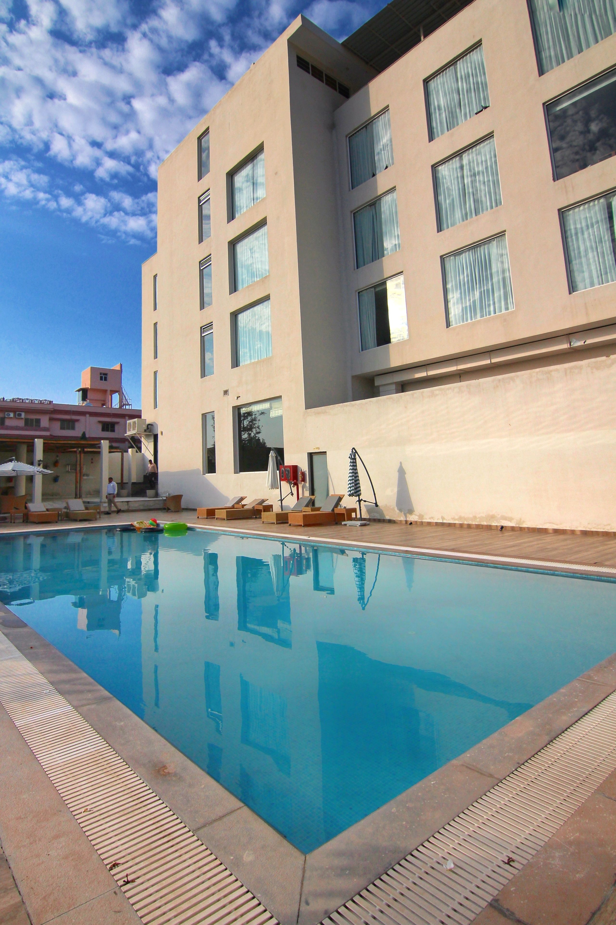 A modern building with a swimming pool, sun loungers, and a covered area with umbrellas.