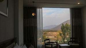 A hotel room with a large window, a bed, two chairs, and a small table. - Brahma Horizon Hotel & Spa – Pushkar (Pushkar)