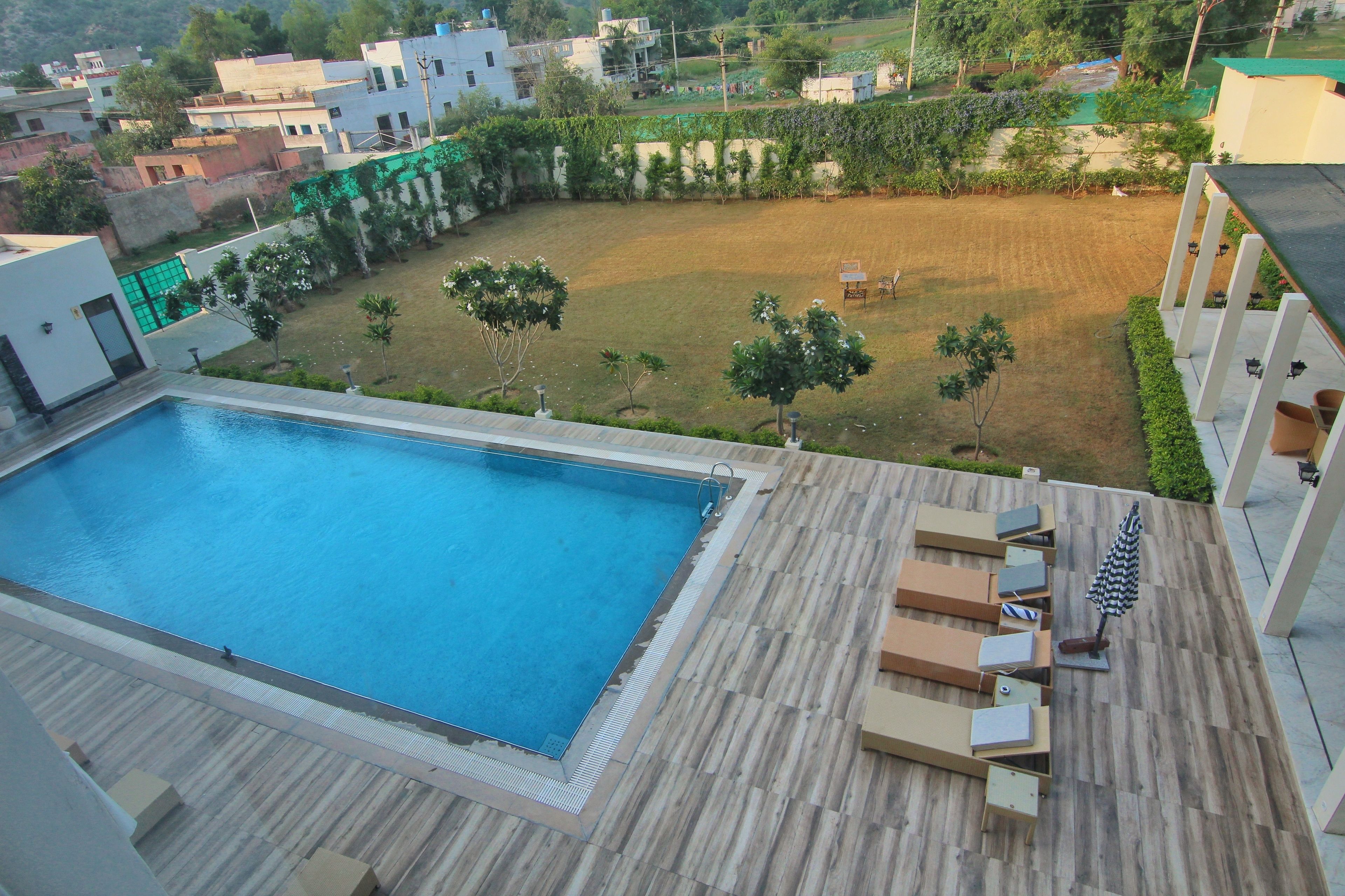 Piscina en la azotea con terraza de madera y sillones de descanso, rodeada de jardín y edificios residenciales.