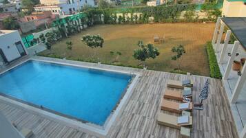 Piscina en la azotea con terraza de madera y sillones de descanso, rodeada de jardín y edificios residenciales.