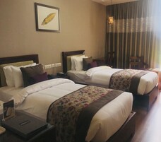 Habitación de hotel con dos camas, cada una con ropa de cama blanca y colchas con estampado floral. Hay una obra de arte enmarcada en la pared sobre las camas y una lámpara colgante.
