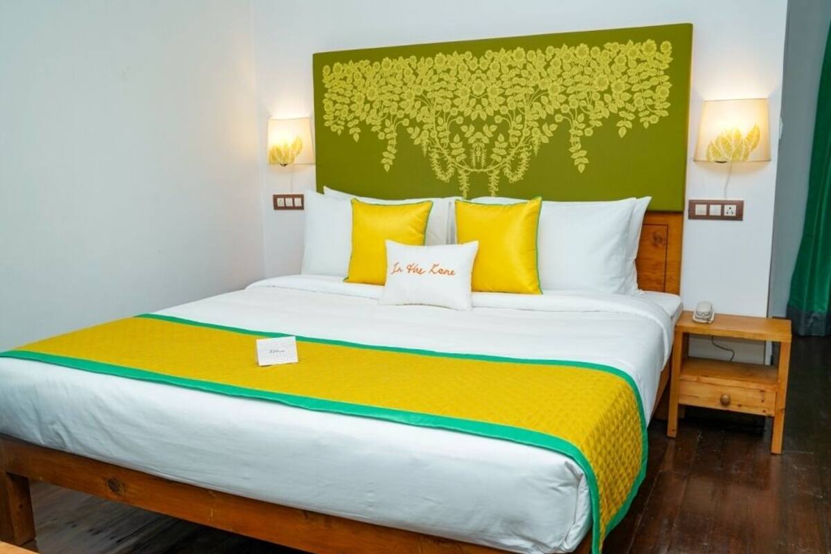 A neatly made bed with a green and yellow bedspread, white pillows, and a green headboard with a floral design.