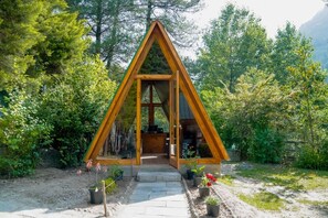A wooden triangular cabin with a glass door, surrounded by lush greenery and a stone pathway leading to it. -  Zone Connect by the Park Manali  (Kullu)
