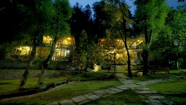 Una casa de dos pisos con fachada de piedra, rodeada de árboles y un camino de piedra que lleva a un banco.
