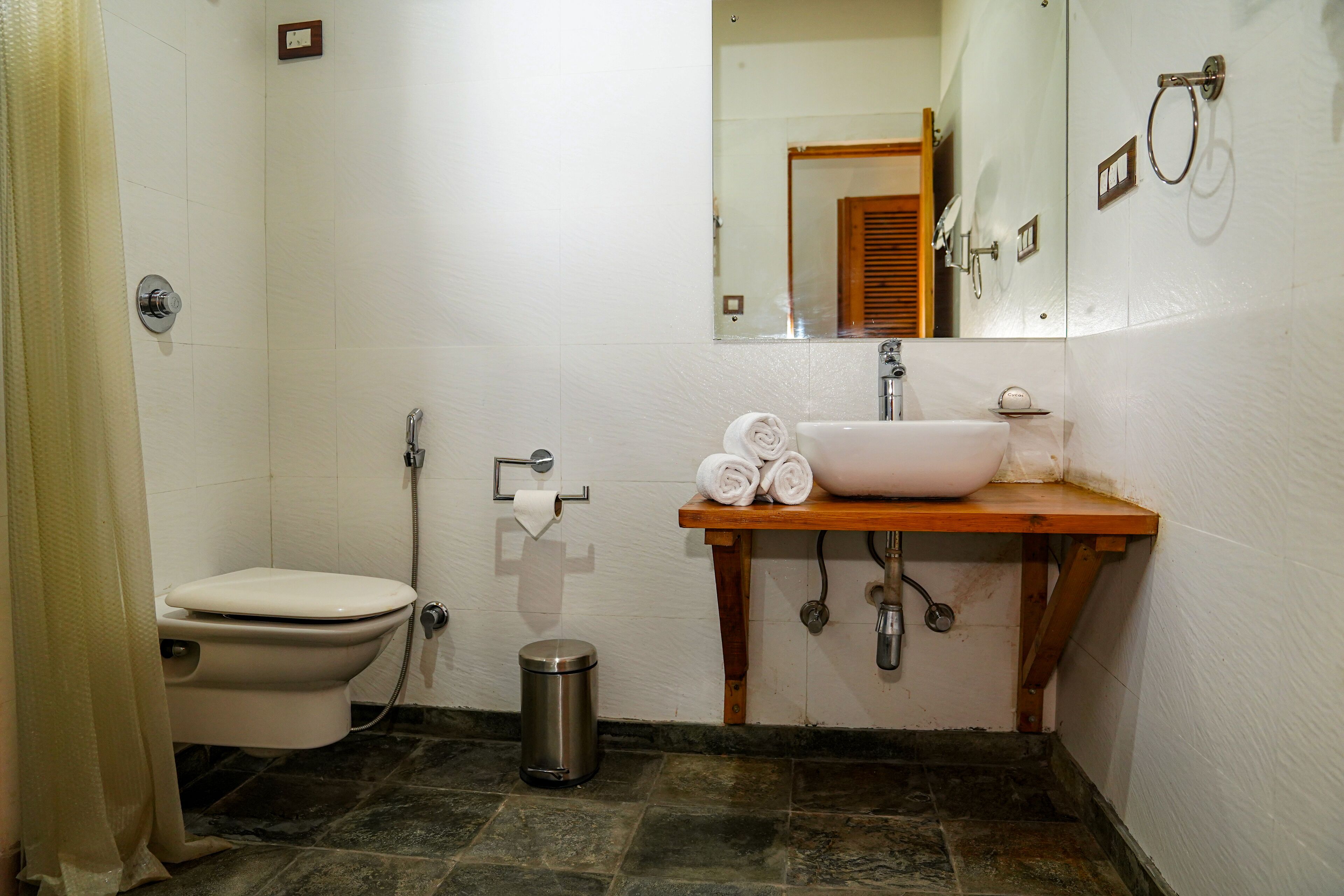 A bathroom with a toilet, sink, mirror, and a trash bin.
