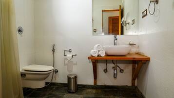 A bathroom with a toilet, sink, mirror, and a trash bin.