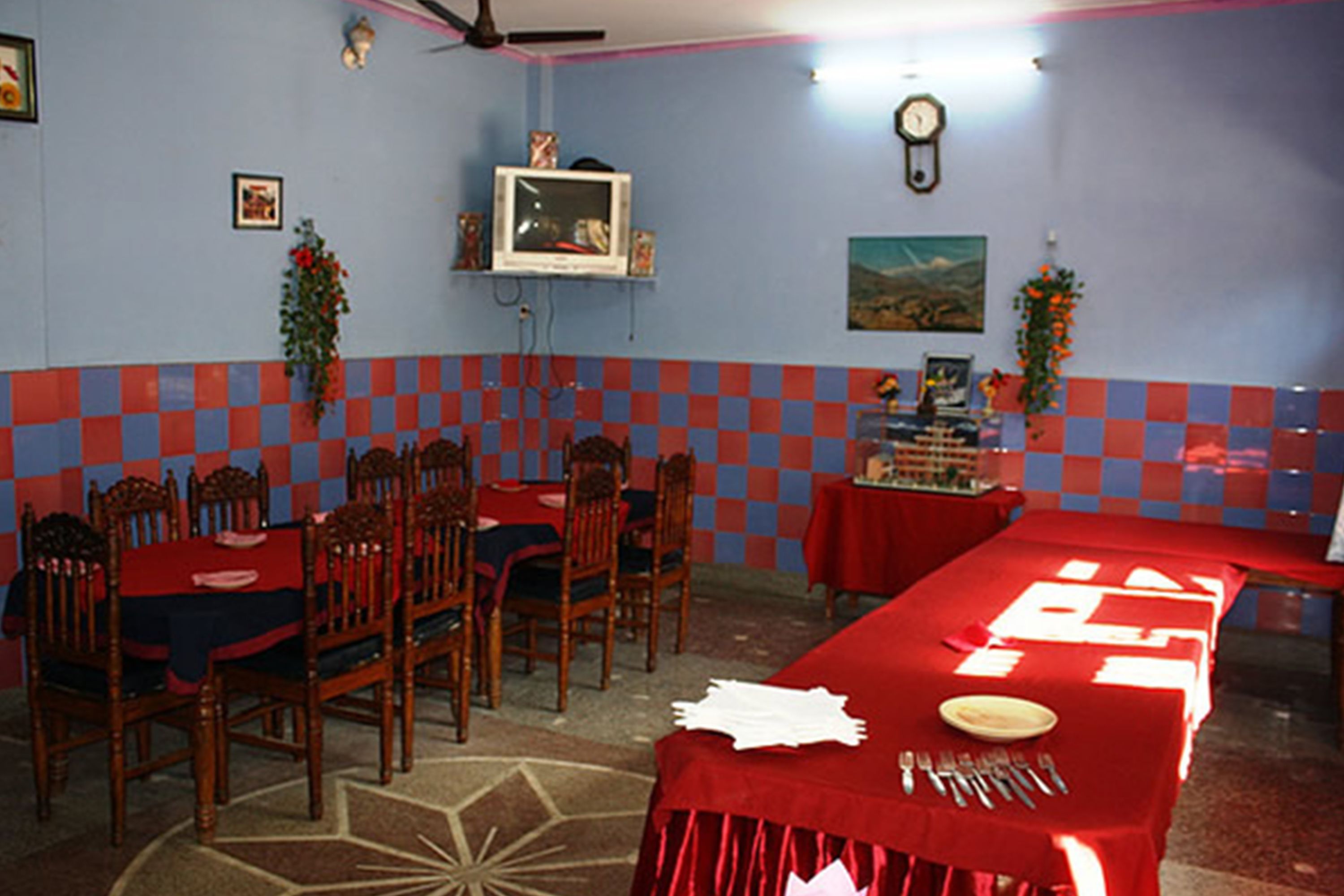 A restaurant with checkered walls, wooden chairs, and tables set with red tablecloths.