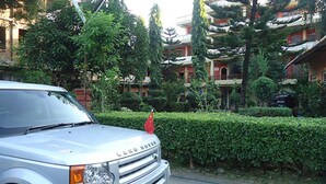A silver Land Rover parked on a street with a red flag on the roof, surrounded by greenery and buildings. - Hotel Peace Palace (Baglung)