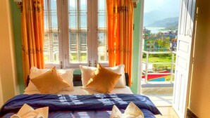 A hotel room with a bed, two pillows, and a balcony with a view of a city and mountains. - Hotel Atrium (Pokhara)