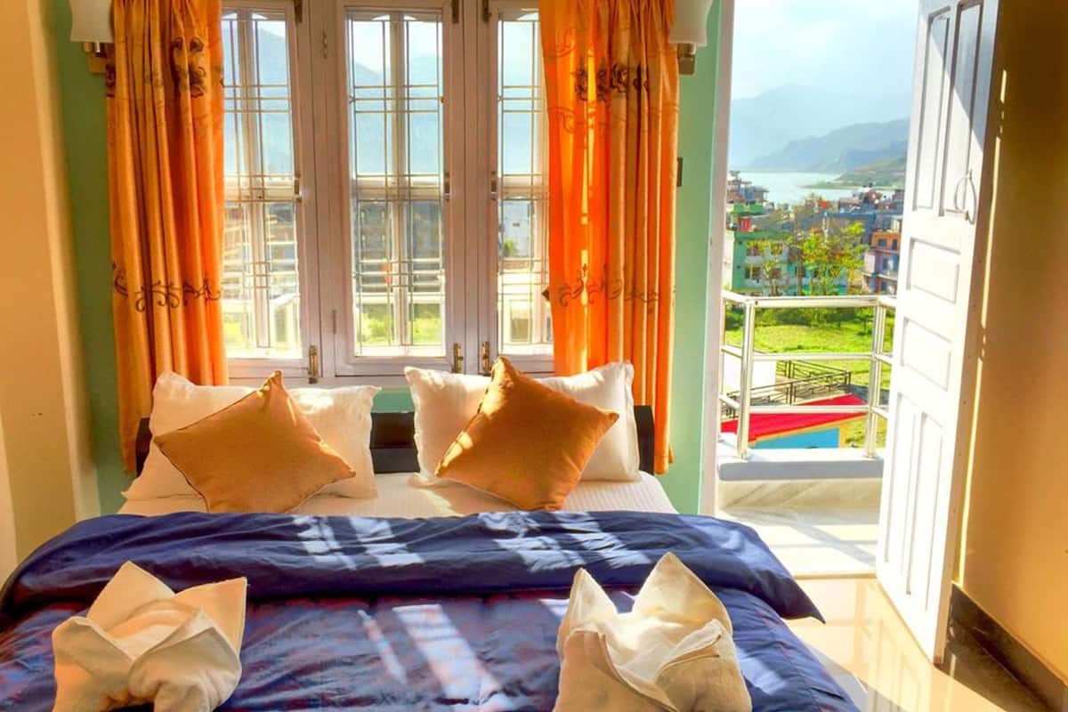 A hotel room with a bed, two pillows, and a balcony with a view of a city and mountains.