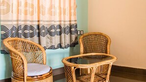 Two wicker chairs with cushions and a small round table, positioned in front of a window with patterned curtains. - Hotel Atrium (Pokhara)