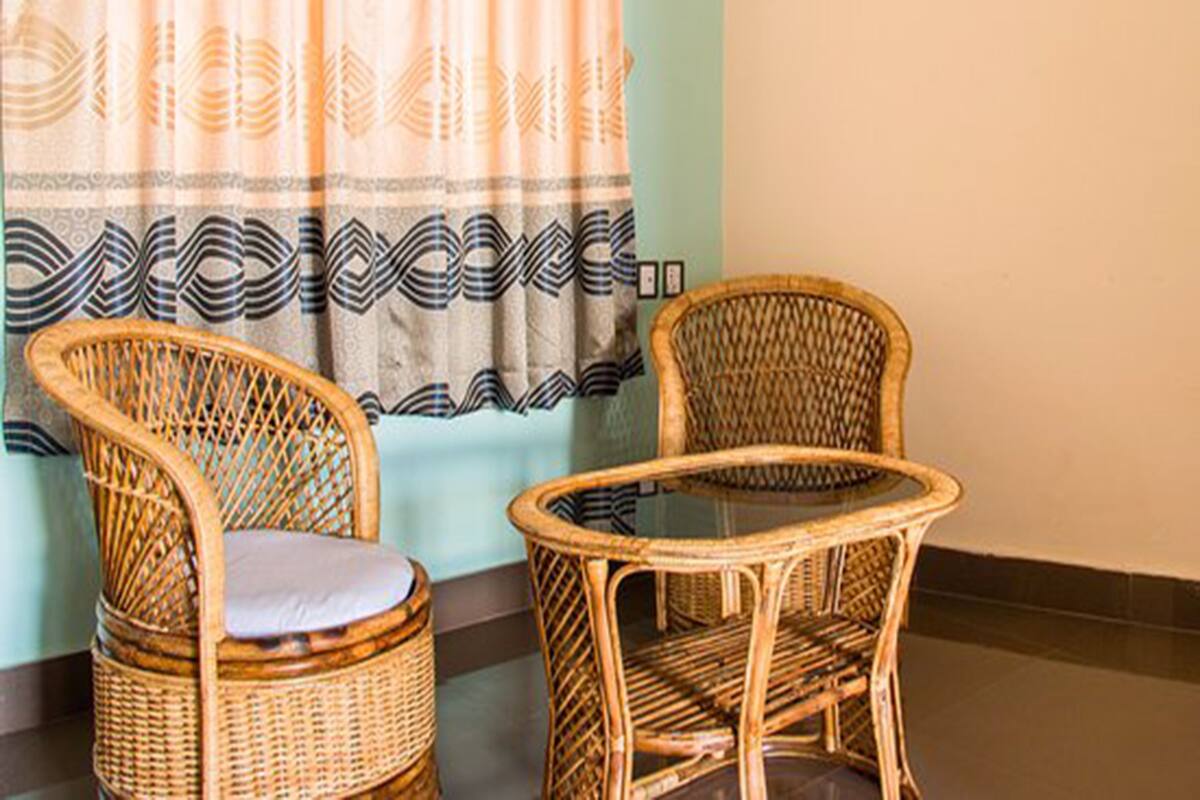 Two wicker chairs with cushions and a small round table, positioned in front of a window with patterned curtains.