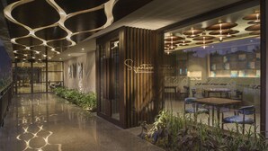 A modern interior with a signature sign, a dining area with tables and chairs, and a reflective floor. - Kabir Hotel & Spa (Vadodara)