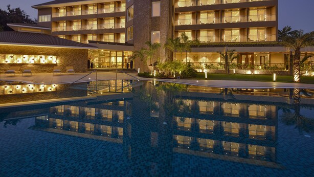 A multi-story hotel with a swimming pool, outdoor seating, and well-lit balconies. - Kabir Hotel & Spa (Vadodara)