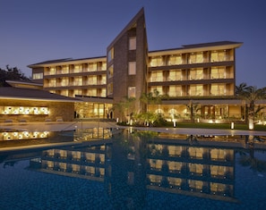 Un hotel de varios pisos con piscina, mobiliario exterior y balcones bien iluminados.